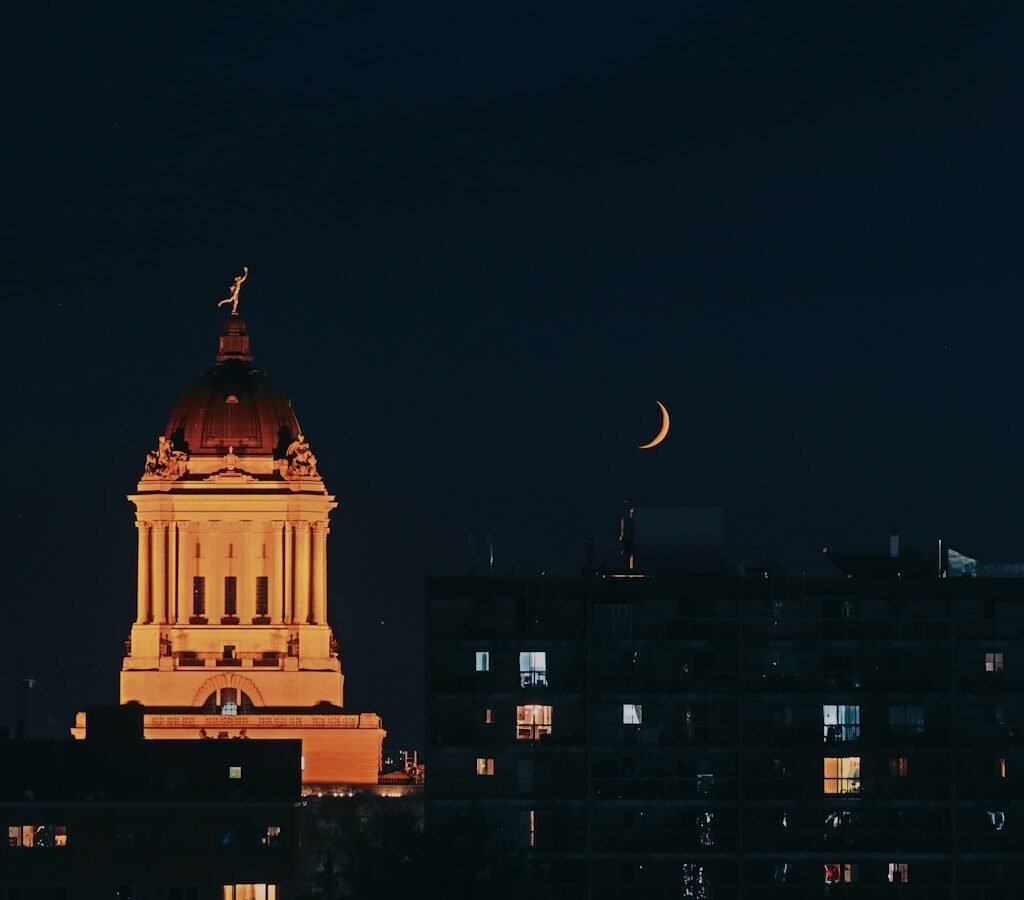 a clock tower lit up at night with the moon in the sky